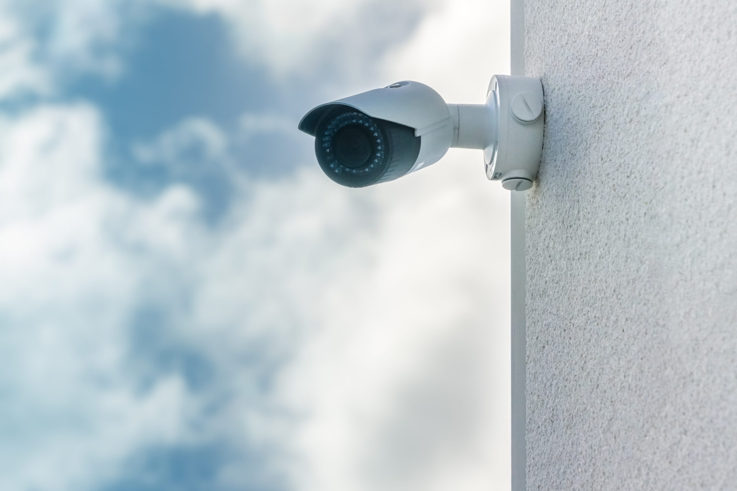 Cctv Security Camera In Front Blue Sky Background Installed On White Building Wall